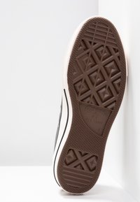 Svart gummisula med en strukturerad yta. Mjuk krämfärgad mellansole med bruna accenter, med sicksackmönster och en cirkulär logotypdetalj.