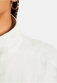 Chemise blanche à col avec une texture lisse et un tissu léger. Présente des coutures minimales et un design de col élégant.