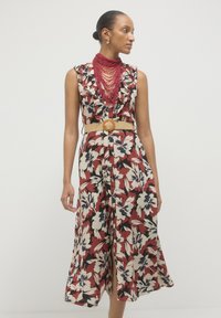 Floral jumpsuit featuring a red, cream, and navy color scheme, with ruffled neckline, wide legs, and a textured beige belt with a circular buckle.
