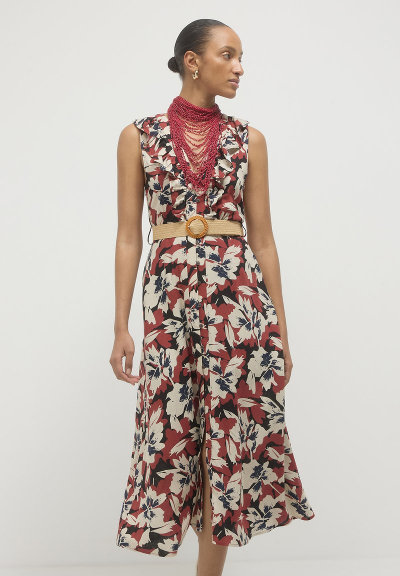 Floral jumpsuit featuring a red, cream, and navy color scheme, with ruffled neckline, wide legs, and a textured beige belt with a circular buckle.
