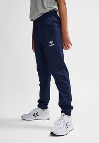 Marine joggingsbroek met een elastische tailleband, zijzakken en witte logo details. Gecombineerd met witte sportschoenen en een grijze T-shirt.