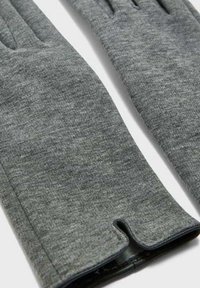 Guanti grigi lavorati a maglia con una superficie liscia, dotati di polsini allungati e di un piccolo dettaglio a taglio alla base.