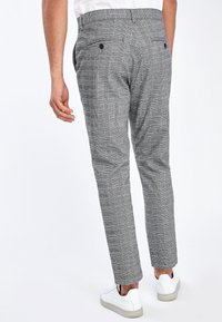 Pantaloni a quadri grigi con una vestibilità sagomata, dotati di due tasche posteriori con bottoni. Il tessuto ha una texture liscia. Indossati con sneakers bianche.