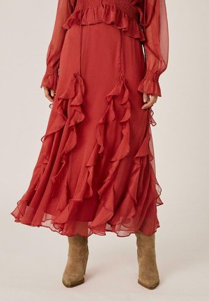 Vestido midi rojo con mangas largas transparentes y volantes en cascada, combinado con botines de ante marrón claro.