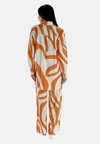 Wit langemouwen shirt en broek set met oranje abstracte patronen. Gladde stof, relaxte pasvorm en met knopen aan de mouwen.