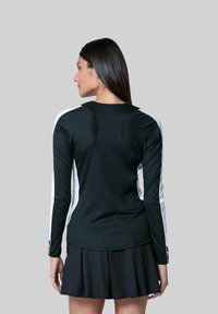 Zwarte top met lange mouwen en witte zijpanelen, ronde halslijn en geribbeld textuur. Gecombineerd met een zwarte flared rok, die een sportieve uitstraling heeft.