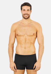 Pantaloni de baie negri pe un model masculin cu un fizic zvelt, având o textură netedă și un design simplu, ajustat.