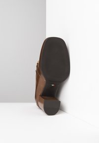 Brązowe skórzane buty na blokowym obcasie z teksturowaną podeszwą i złotymi akcentami. Obcas ma eleganckie drewniane wykończenie.