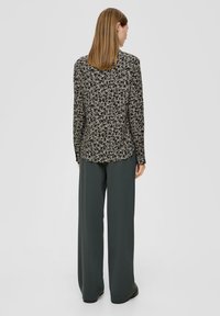 Zwart bloemenblouson met lange mouwen en een gebogen zoom, gecombineerd met hoge, wijde, donkergroene broeken, met een gladde stofstructuur.