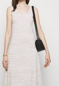 Abito senza maniche color beige chiaro con scollo rotondo e lavorazione a maglia testurizzata. Abbinato a una piccola borsa nera con una lunga tracolla e dettaglio triangolare.