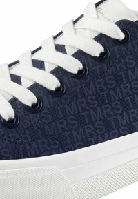 Marineblaue Canvas-Sneaker mit weißen Schnürsenkeln, ausgestattet mit einer strukturierten Oberseite, die mit dem Wort "TMRS" geprägt ist, und einer weißen Gummisohle.
