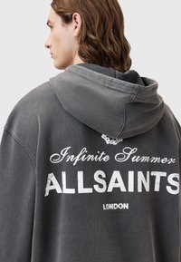 Szara bluza z kapturem, z białym napisem "Infinite Summer ALLSAINTS LONDON" na plecach, o luźnym kroju i bawełnianej fakturze.