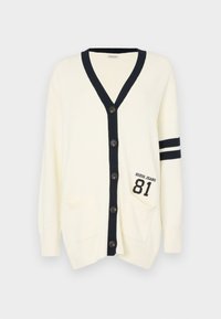 Kremowy sweter na drutach z granatowymi akcentami, dekolt w serek, zapinany na guziki, z dwiema kieszeniami oraz haftem "Guess Jeans 81" z przodu.