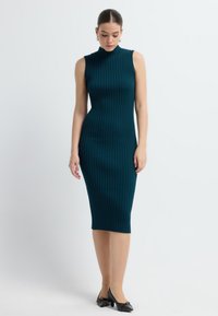 Vestito teal a coste con scollatura alta, design senza maniche e forma aderente. Presenta un tessuto testurizzato e arriva fino a metà polpaccio.