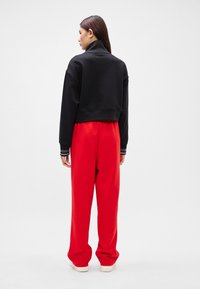 Black cropped sweatshirt with a high collar and red sweatpants, featuring a loose fit and cuffed ankles, paired with white sneakers.