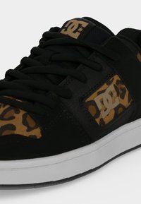 Baskets noires avec des accents imprimé léopard marron et une semelle blanche, avec le logo DC sur le côté et la languette, avec des lacets noirs attachés.