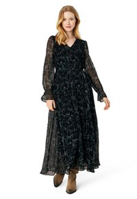 Long black dress with sheer long sleeves, v-neckline, pleated skirt, and floral pattern. Paired with ankle-height brown boots.