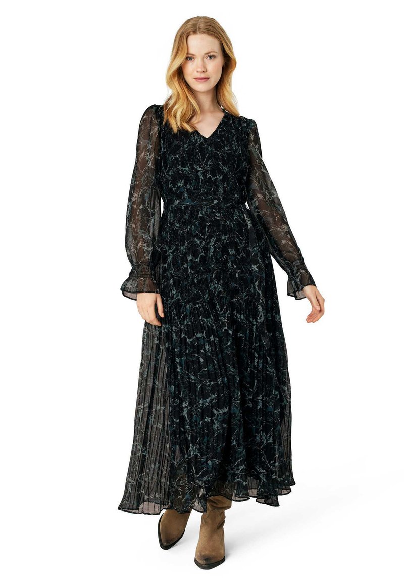 Long black dress with sheer long sleeves, v-neckline, pleated skirt, and floral pattern. Paired with ankle-height brown boots.