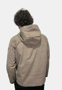 Giacca in cotone beige chiaro con cappuccio, cuciture visibili e vestibilità rilassata. La vista posteriore mostra un design pulito senza loghi visibili.