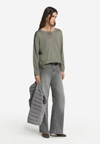 Grå långärmad tröja, lös passform, med ribbade ärmavslut, ihop med vida grå jeans. Håller en vadderad grå jacka, bruna skor.