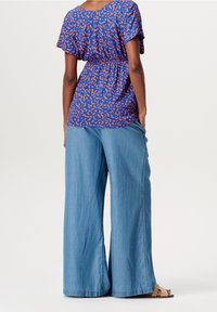 Blue patterned blouse with orange abstract design, paired with light blue wide-leg jeans. Material appears lightweight and breathable.