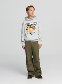 Felpa grigia con grafica "STUMBLE GUYS" in nero e giallo, abbinata a pantaloni a gamba larga verde oliva e scarpe nere con suole marroni.