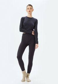 Mørk ribbet langærmet top parret med matchende tætsiddende leggings. Modellen bærer lyse beige strukturerede sokker, hvilket skaber et hyggeligt lag-på-lag look.