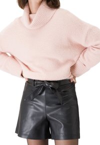 Helles rosa, flauschiges Strickpullover mit einem gerippten Kragen, kombiniert mit hochgeschnittenen schwarzen Leder-Shorts mit einer gebundenen Schleifendetail.