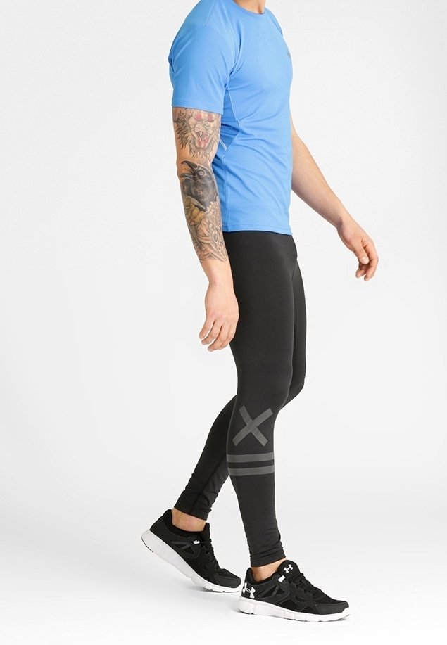 Svarta träningsbyxor med grå ränder, i kombination med en kortärmad blå skjorta och svarta sneakers, med en slät textur och en kroppsnära design.