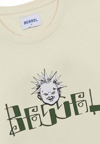 Camiseta de algodón color crema con un diseño gráfico verde que presenta un personaje con pelo puntiagudo y el texto "BESSEL" en una fuente negrita y estilizada.