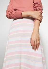 Ljusrosa sweatshirt med ribbade ärmar, kombinerad med en randig kjol. Kjolen har horisontella ränder i rosa, beige, ljusblå och vit.