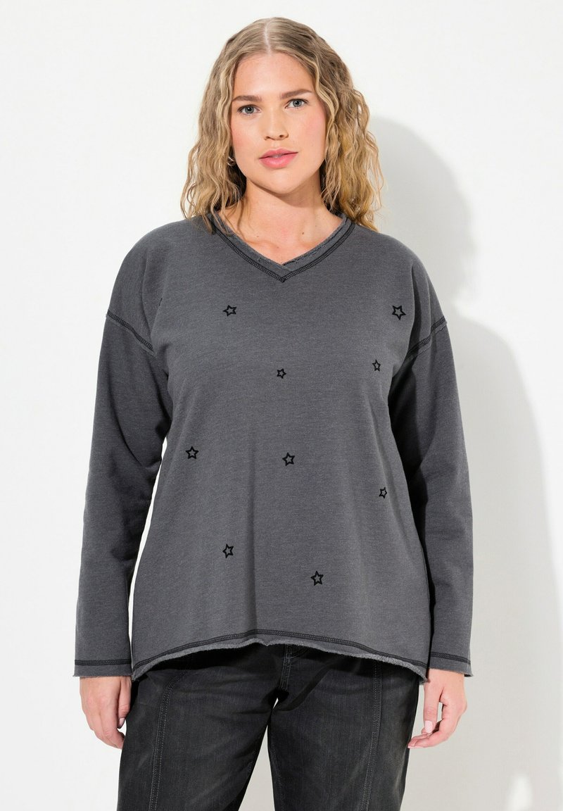 Suéter gris de manga larga con escote en V, con bordado de estrellas negras por todo el diseño y un dobladillo ligeramente curvado. Textura de tela suave.