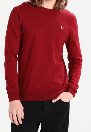 Rode trui van gebreide stof, met een ronde halslijn en lange mouwen. Een klein wit logo is zichtbaar op de linkerborst.