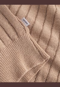 Beige kudumi, millevertikaalne sooniktekstuur, lahtine kude ja väike silt, millel on kirjad "LES DEUX". Pehme puuvillasegune materjal.