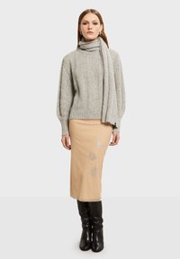 Šedý pletený svetr s vysokým límcem, spuštěný s béžovou tužkovou sukní s stříbrnými květinovými ozdobami. Černé kozačky po kolena dokončují vzhled.