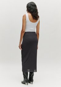 Schwarzer Rock mit Pünktchenmuster und einem taillierten weißen Oberteil. Der Rock hat eine elegante Silhouette, die bis zur Mitte der Waden reicht, kombiniert mit schwarzen High-Heels-Stiefeln.
