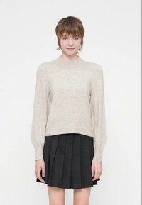 Svetlo bež pulover iz mehke tkanine z okroglim izrezom, dolgimi napihnjenimi rokavi in oprijetim robom, kombiniran s temno plisirano krilo.