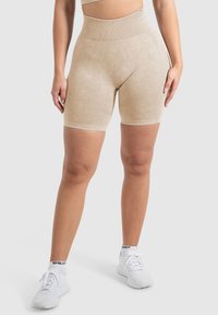 Pantaloni corti beige a vita alta con un tessuto liscio e textured e linee sottili. Abbinati a scarpe sportive bianche con dettagli neri.