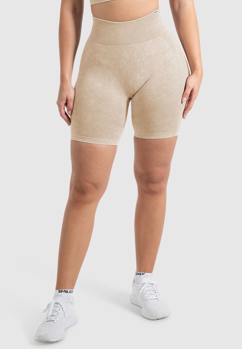 Pantaloni corti beige a vita alta con un tessuto liscio e textured e linee sottili. Abbinati a scarpe sportive bianche con dettagli neri.