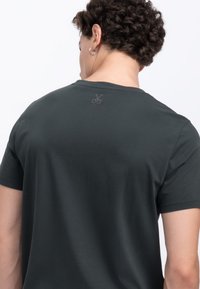 Donkergrijze T-shirt met korte mouwen, voorzien van een discreet schaarlogo op de achterkant van de halslijn, gemaakt van een glad, lichtgewicht materiaal.