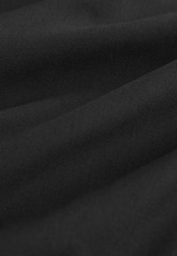 Schwarzer Stoff mit einer glatten Textur, der ein mattes Finish und ein dezentes Webmuster aufweist, gefaltet, um Schichten und Tiefe zur Geltung zu bringen.