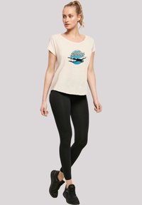 Cream short-sleeve t-shirt with a blue and black graphic design featuring an airplane, paired with black leggings and black sneakers.