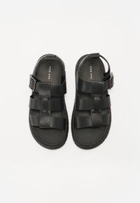 Sandales noires avec un design tissé, fabriquées en matériau lisse. Équipées d'une boucle réglable et d'une semelle texturée pour une meilleure adhérence.