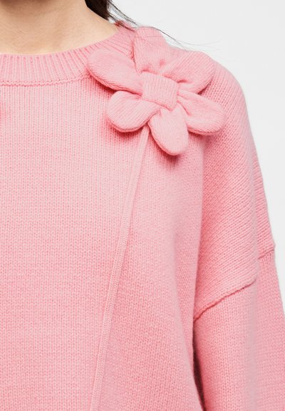 Ροζ πλεκτό πουλόβερ με μεγάλο λουλουδένιο απλικέ στον αριστερό ώμο, σε άνετη γραμμή με ριμπ λαιμόκοψη και μανσέτες.