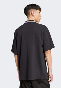 Black short-sleeve polo shirt with a contrasting striped collar, relaxed fit, made of smooth fabric, showcasing a plain back design.