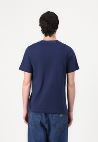 T-paita, jossa on lyhyet hihat ja tummansininen väri, valmistettu puuvillasta, perinteisellä pyöreällä kauluksella. Takakatsaus, joka osoittaa rennon istuvuuden.