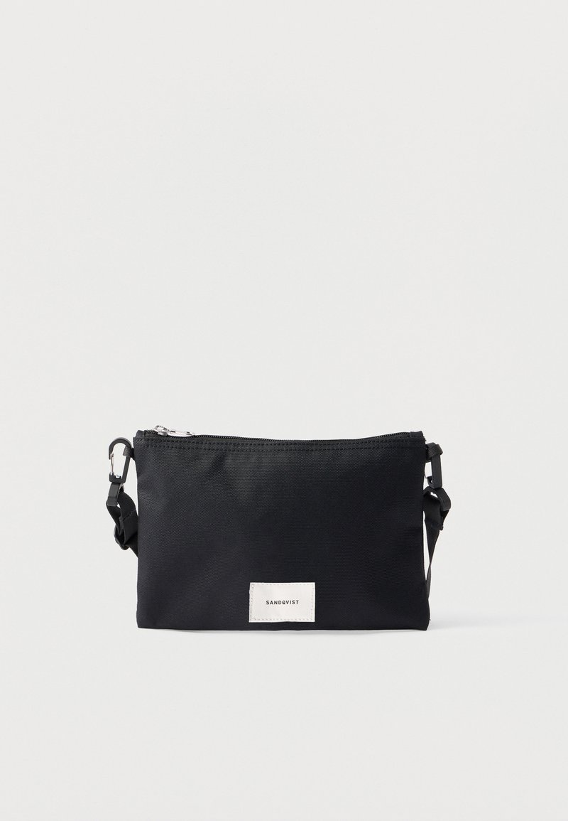 Čierna textilná kabelka cez rameno so zipsovým uzáverom, nastaviteľným popruhom a bielou značkovou etikietou na prednej strane. Jednoduchý obdĺžnikový dizajn.