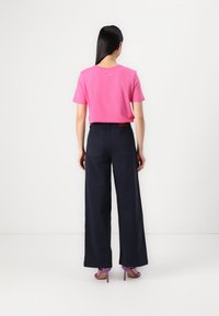 T-shirt de algodão rosa com mangas curtas, combinado com calças largas azuis-marinho e sandálias roxas de salto alto. Design simples, sem padrões.