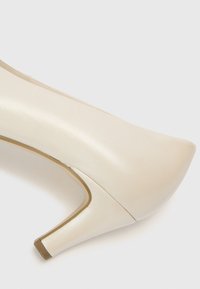 Μπεζ γυναικείο παπούτσι με ψηλό τακούνι και μυτερή μύτη, κατασκευασμένο από υφή δερματίνης με κωνικό τακούνι και λεία επιφάνεια.