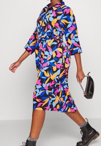 Färgglad klänning med blommönster i svart, med krage, trekvartsärmar och åtdragen midja. Bärs med mörka stövlar.